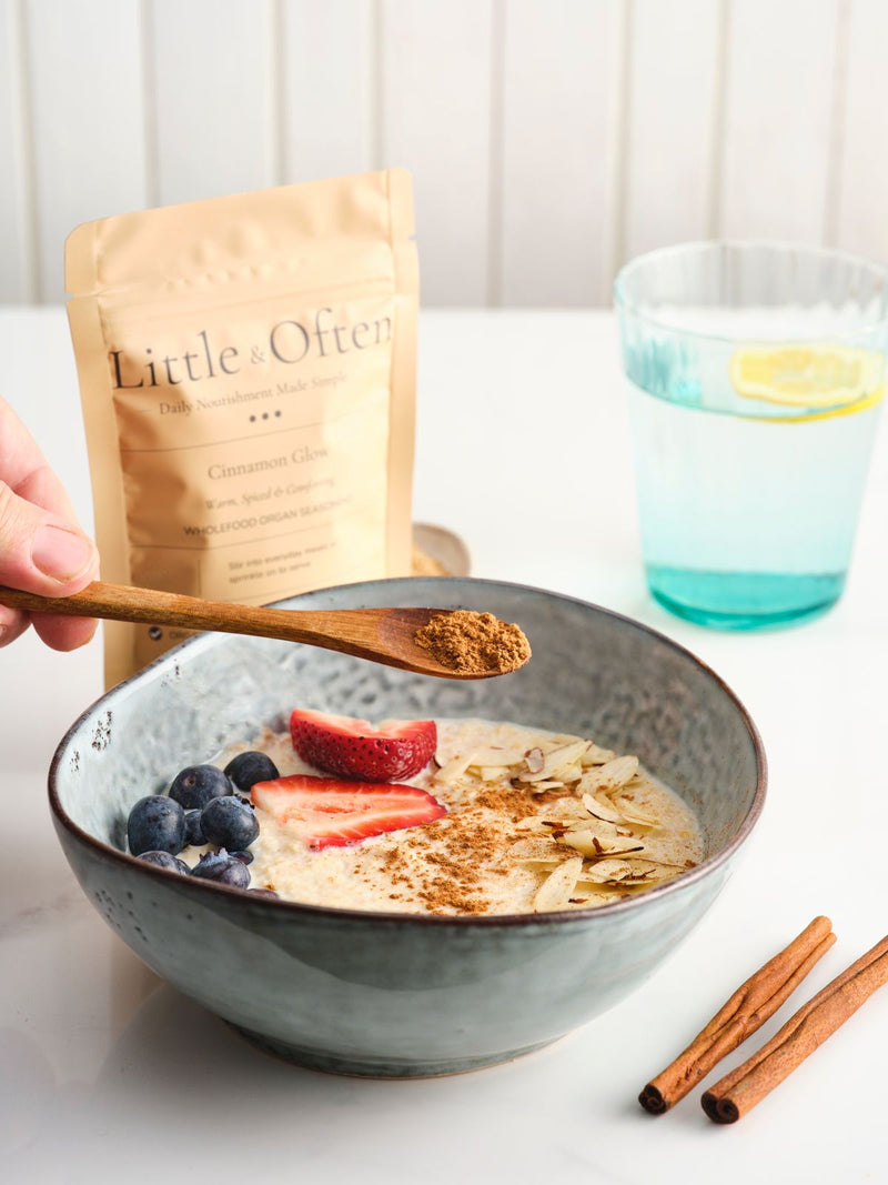 Spoon of Little & Often Cinnamon Glow seasoning held over porridge topped with strawberries, blueberries and flaked almonds.